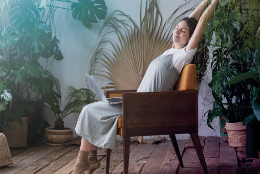 Femme assise dans un fauteuil, se relaxant les bras levés au milieu de plantes d’intérieur